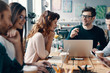 © gstockstudio - Young business professionals. Group of young modern people in smart casual wear discussing something and smiling while working in the creative office