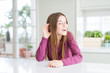 © Krakenimages.com - Beautiful young girl kid on white table smiling with hand over ear listening an hearing to rumor or gossip. Deafness concept.