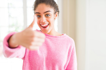 Beautiful young african american woman with afro hair doing happy thumbs up gesture with hand. Approving expression looking at the camera showing success.