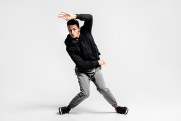 Wall Mural - Stylish young man wearing a black sweatshirt and gray pants is dancing  street dances on a white background