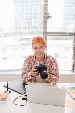 Smiling photo editor working on computer at desk with camera and graphics tablet