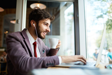 Young man at cafe drinking coffee and working on laptop