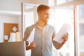 Waist up portrait of handsome young man holding documents standing by window in sunlight, copy space