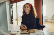 © Flamingo Images - Smiling young businesswoman using a cellphone at her office desk
