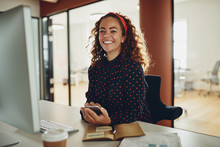 Smiling Young Businesswoman Using A Cellphone At Her Office Desk