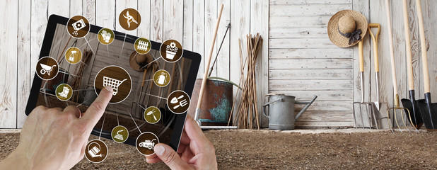 gardening equipment e-commerce concept, online shopping on digital tablet, hand pointing and touch screen with garden tools icons, tool shed in the background