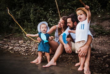 Wall Mural - A young family with two toddler children outdoors by the river in summer.