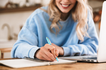 Poster - Portrait of european blond woman 20s wearing casual sweatshirt working on laptop and writing down notes at home