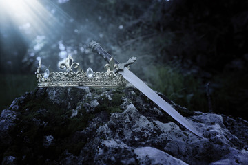 mysterious and magical photo of gold king crown and sword in the England woods over stone covered with moss. Medieval period concept