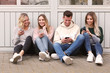 Leinwandbild Motiv Vier junge Leute mit Handys sitzen an eine Wand gelehnt
