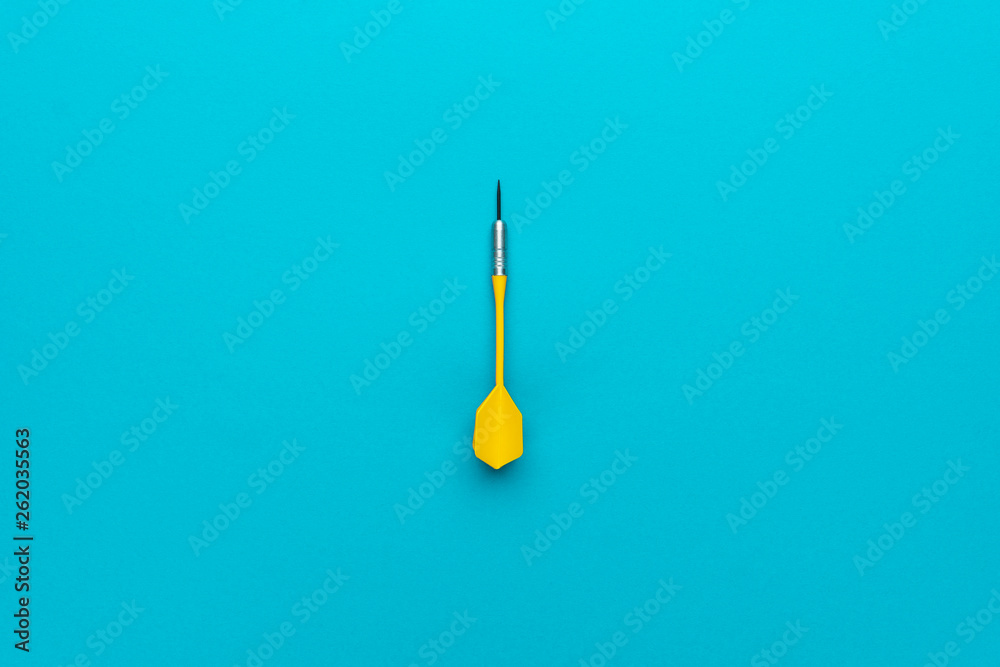 minimalist photo of yellow plastic dart with metal tip on blue background - obrazy, fototapety, plakaty 