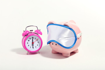 Poster - Piggybank with sleeping mask and alarm clock on white background. Minimalism concept