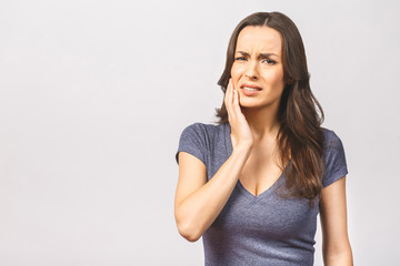 Young European woman isolated on white background suffering from severe toothache, feeling pain so strong that she is pressing fingers to cheek to calm it down, looking desperate.