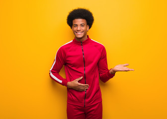 Wall Mural - Young sport black man over an orange wall holding something with hand