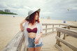 © prostooleh - A young redheaded girl in a large round hat and white shirt standing on the sand on the beach