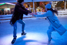 Happy Young Couple Ice Skating On An Ice Rink At Night