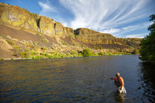 A Man In Waders Fly Fishes The Deschutes River In Oregon At Sunset.