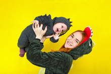 Mom And Daughter In A Funny Dragon Costume. Play On A Yellow Background. Funny
