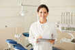 © Seventyfour - Waist up portrait of confident female dentist smiling at camera holding tablet with dental chair in background, copy space