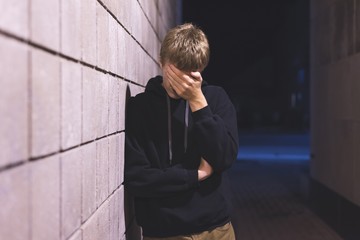 Wall Mural - Upset teenager leaning against a brick wall in an alleyway. He is suffering from depression.