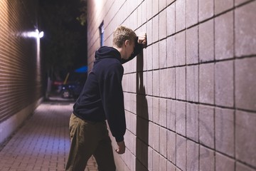 Wall Mural - Upset teenager leaning against a brick wall in an alleyway. He is suffering from depression.