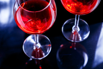 Two Glasses of red wine in bar, night club on black background with reflection.