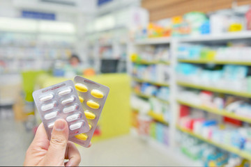 Wall Mural - Pharmacist holding medicine capsule pack on blur pharmacy store background