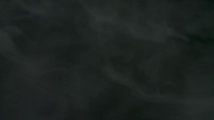 Poster - Smoke fragments flowing on black background. Stock footage. Beautiful white clouds of smoke moving slowly isolated on dark background.