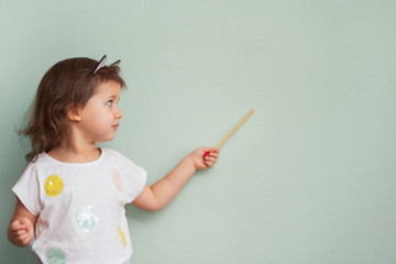 cute Child girl 3 years old with pouting lips and interesting emotion shows to the side and holds a pointer, close-up, portrait, day