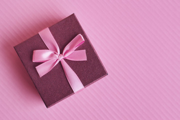 Small purple gift box with pink ribbon on colorful pink background, top view