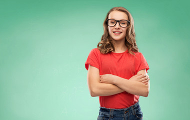 Wall Mural - education, school and people concept - smiling teenage student girl in glasses and red t-shirt with crossed arms over green chalk board background