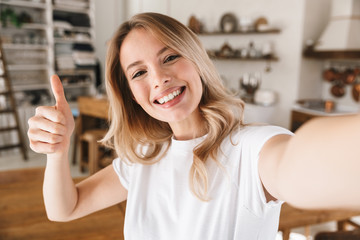 Poster - Image closeup of cheery blond woman showing thumb up while taking selfie photo at home