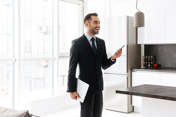 Poster - Image of happy businessman using mobile phone while working on laptop in bright apartment