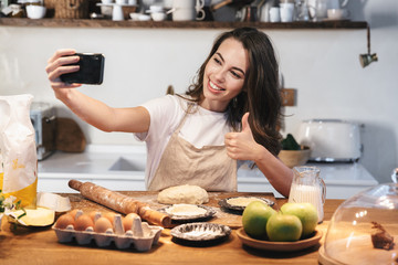 Wall Mural - Cheerful young woman wearing apron preparing dough