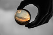 © Vladimir Arndt - Hand holds glass ball which reflects sunset sky over city.