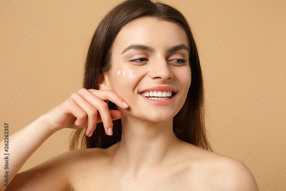Close up half naked woman 20s with perfect skin nude make up applying facial cream isolated on beige pastel wall background, studio portrait. Healthcare cosmetic procedures concept. Mock up copy space - obrazy, fototapety, plakaty 