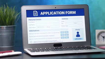 Laptop computer with an application form on its display. Camera turning slowly around the desk.