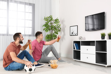 Wall Mural - Young men watching TV while sitting on floor at home. Sport channel