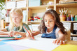 © Comeback Images - Two lovely girls sitting at table and drawing with colored pencils while attending art class in school