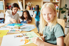 Adorable Albino Girl Smiling And Looking At Camera While Sitting At Table And Painting Nice Picture During Lesson In Art School