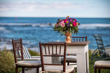 An Antique Table And Chairs With A Beautiful Bouquet Of Flowers In A Vase With The Ocean In The Background