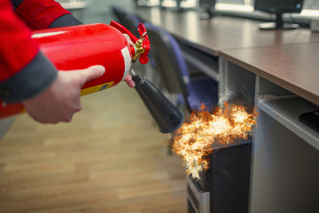 Wall Mural - a man practices how to use a powder type extinguisher in the office. the rescuer puts out the comput