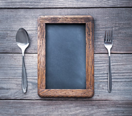 fork and spoon on a rustic table with rough frame for chalk records, blackboard next to the dining utensils