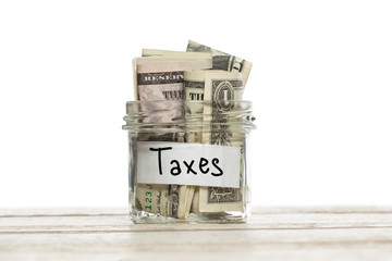 Saving glass jar with money for taxes on wooden table against white background