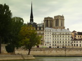 Fototapeta Paryż - Panorama brzegu Sekwany w Paryżu z widokiem na zabytkowe budynki, za nimi dwie wieże i iglica katedry Notre Dame na tle zachmurzonego nieba, stylizowany na akwarelę