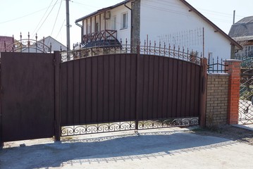 brown metal gate with a forged pattern and part of the fence on the street