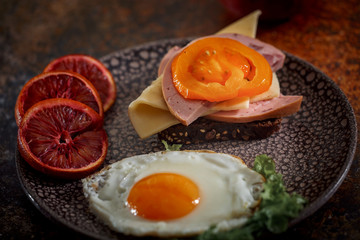 Grain bread with fried egg, tomato, cheese and bacon on ceramic plate with red orange 