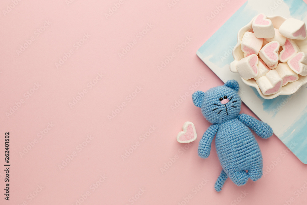 A small knitted baby toy-cat, nitebook and sweetness marshmallow on pink pastel background, flat lay, top view, copy space - obrazy, fototapety, plakaty 