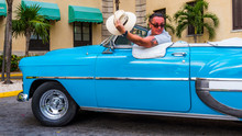 Havana Cuba, Cab Driver Sitting In His Old American Car, Hat Down, Waiving At Some Woman In Front Of A Luxury Hotel. Citizens Of Havana Are Called Habanero In Spanish.