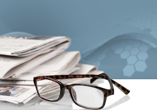 Newspapers with reading glasses on background